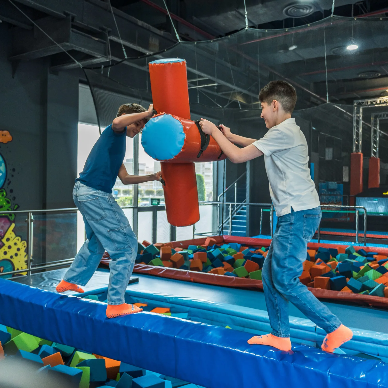 Two boys facing off on Battle Beam over the foam pit at Trampo Kuwait