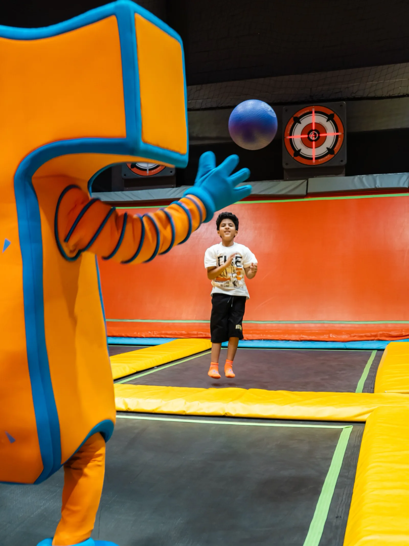 Kid mid-air on the trampoline catching a ball thrown by the Trampo mascot