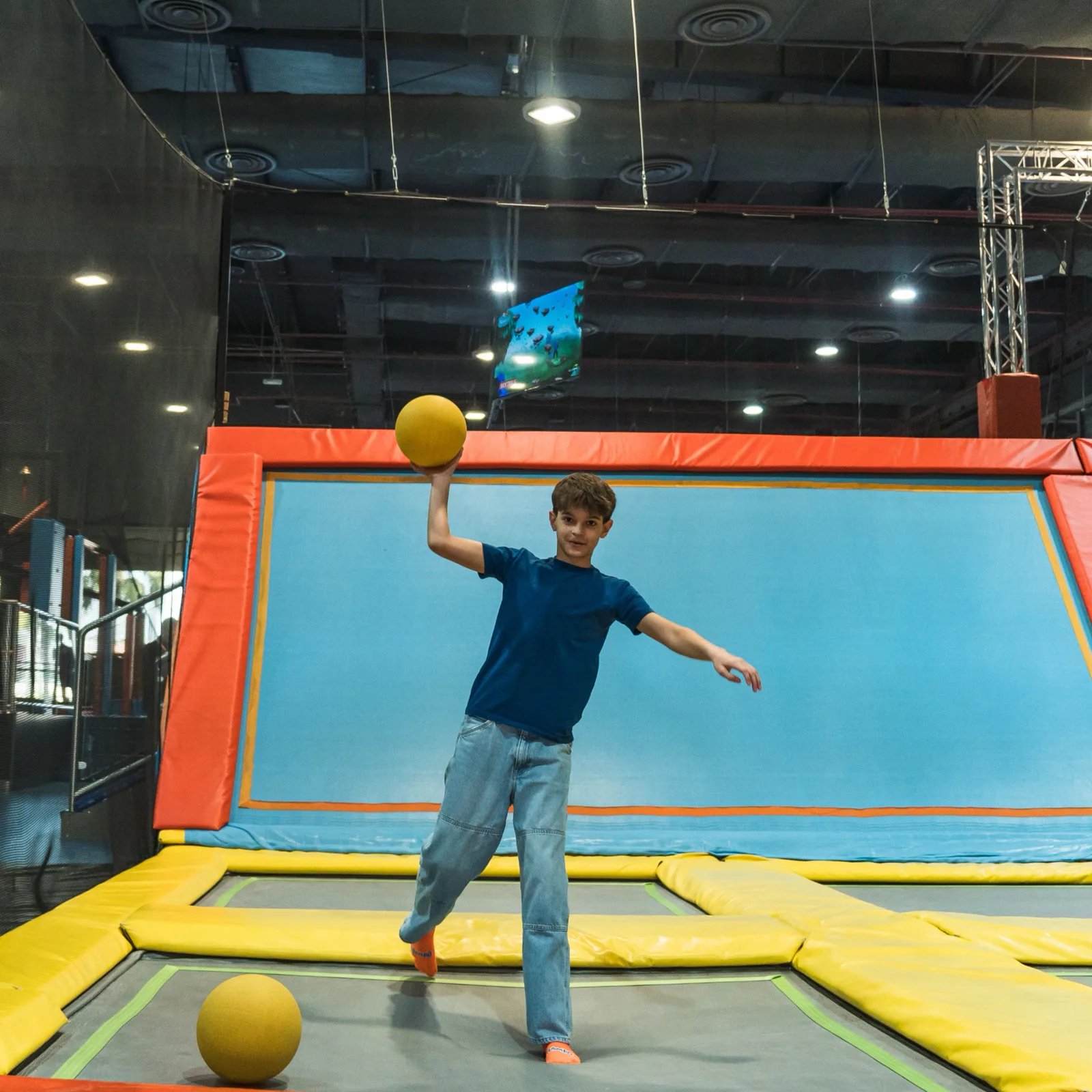 Boy winding up to throw a yellow dodgeball on the trampoline court