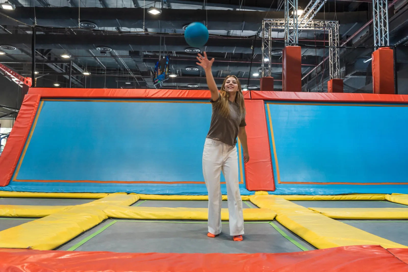 Girl launching a blue dodgeball across the padded trampoline court