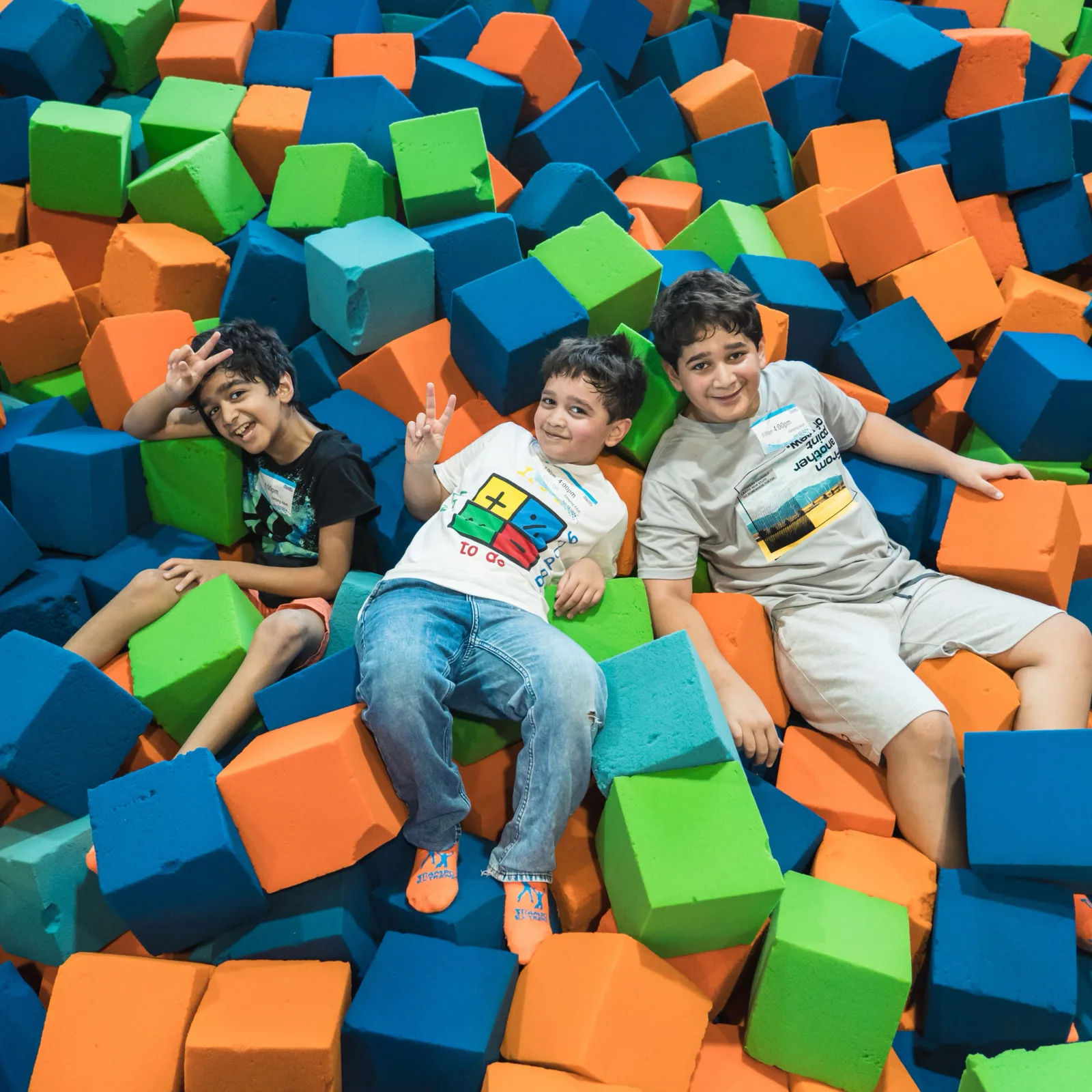 Three kids smiling and posing in the colorful foam cubes at Trampo Kuwait