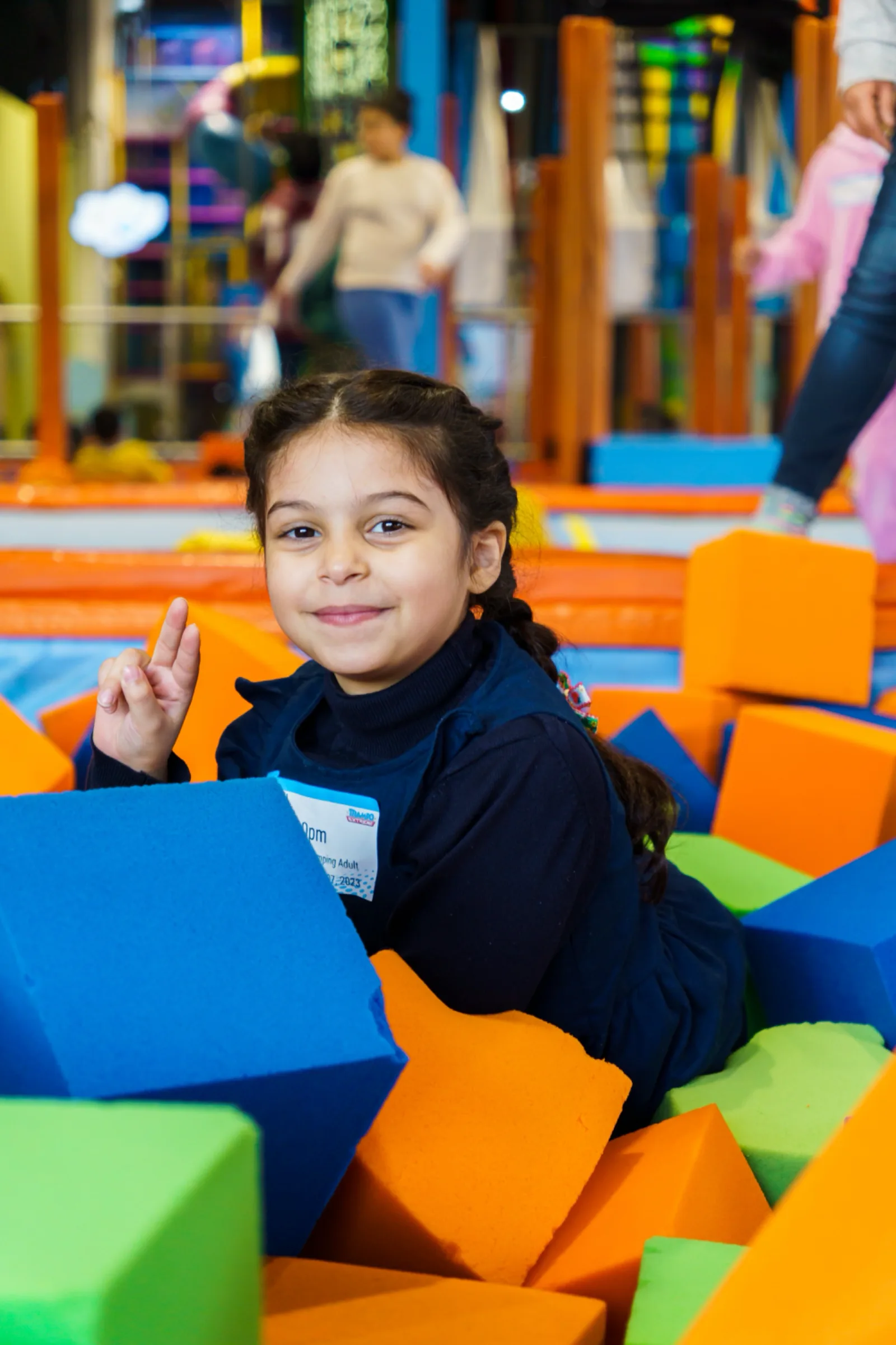 Girl peeking out from a heap of orange and blue foam cubes at Trampo Kuwait