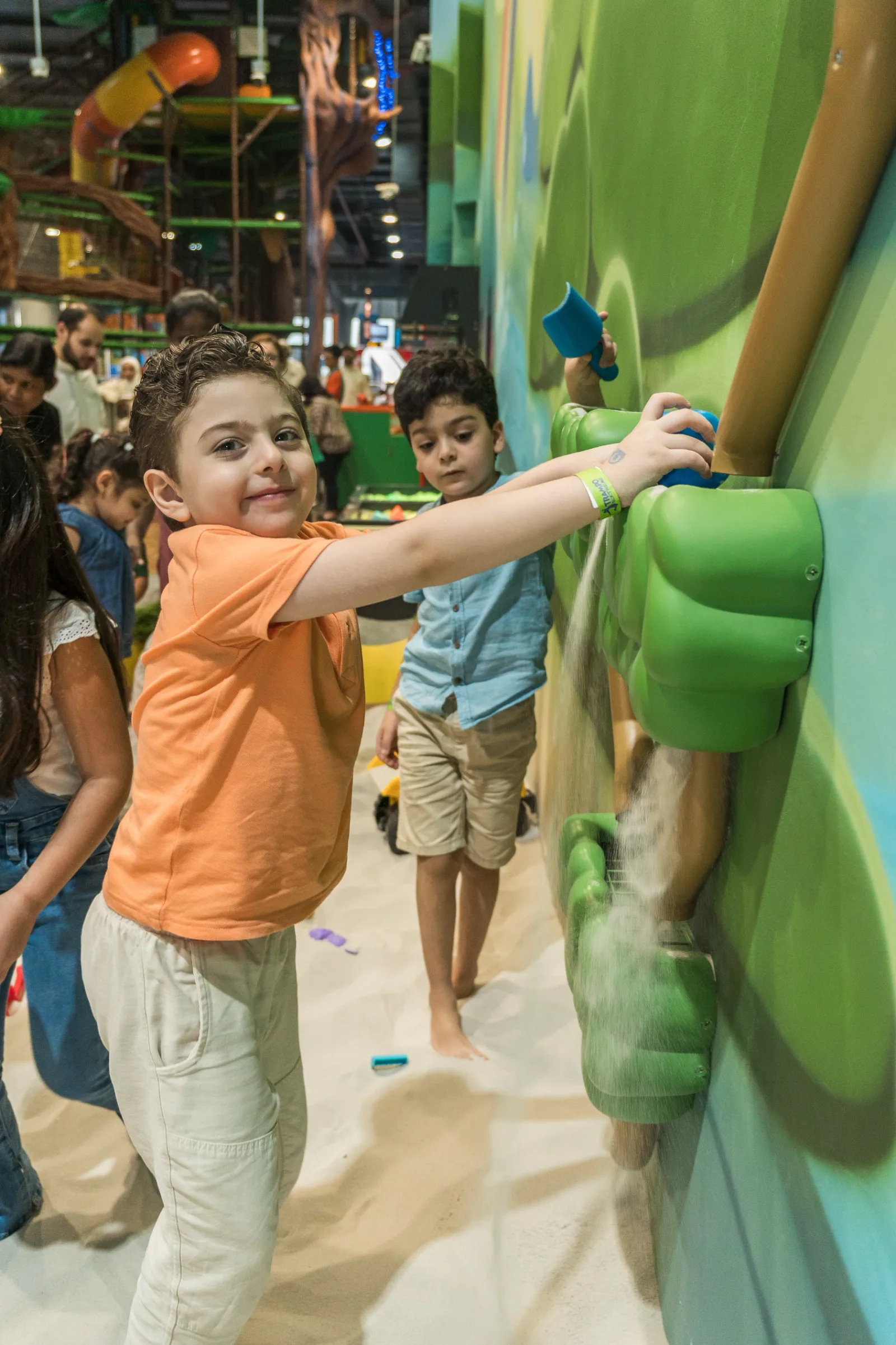 Two boys feeding sand into the wall-mounted green sand mill at the indoor Sand Pit