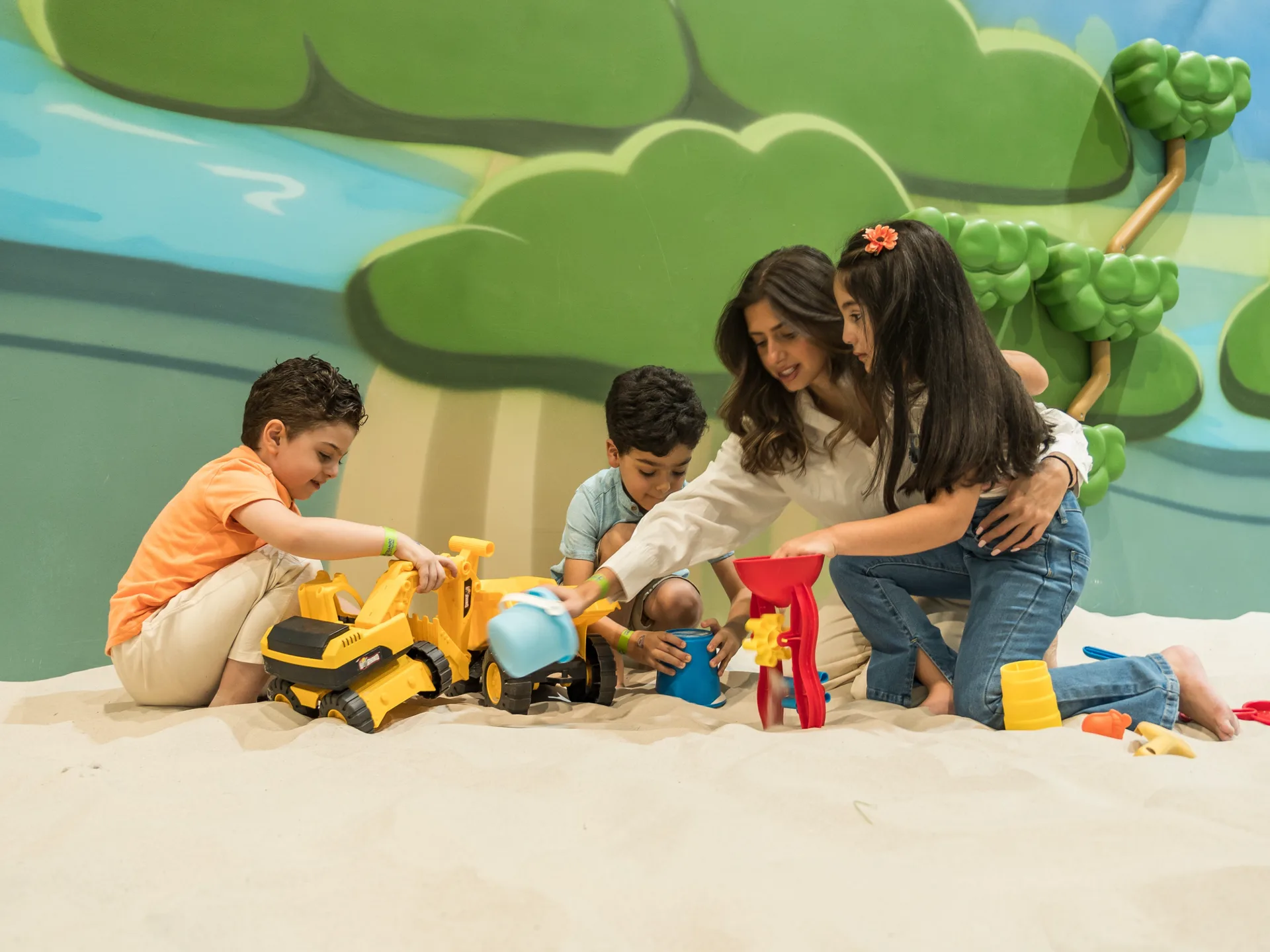 Mum and three kids digging together with bulldozer toys and a sand mill in the indoor Sand Pit at Trampo Messilah Beach
