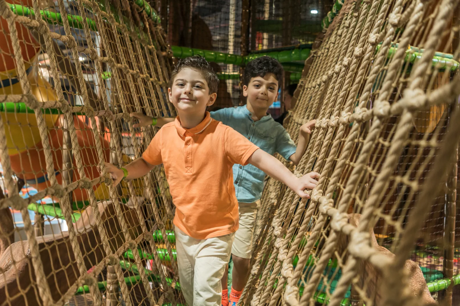 Two boys racing through the rope-net bridge inside the Soft Play tree house