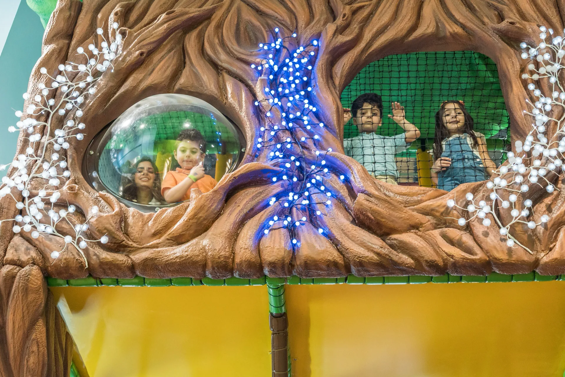 Sculpted tree facade of the Soft Play tree house with kids peeking from the windows at Trampo Kuwait