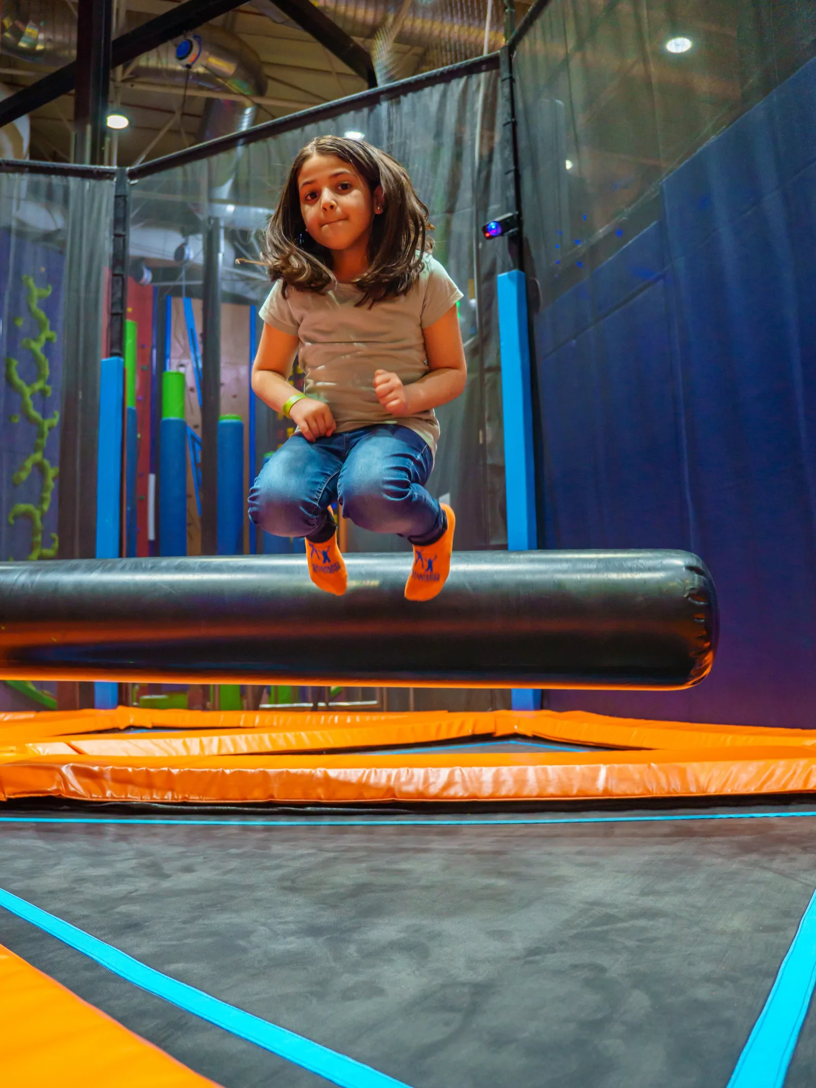 Girl tucking her knees as she jumps over the padded sweeper bar