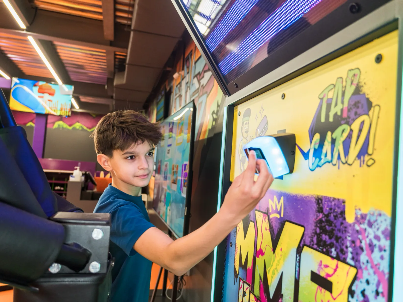 Boy tapping his game card on the reader of a graffiti-styled arcade cabinet