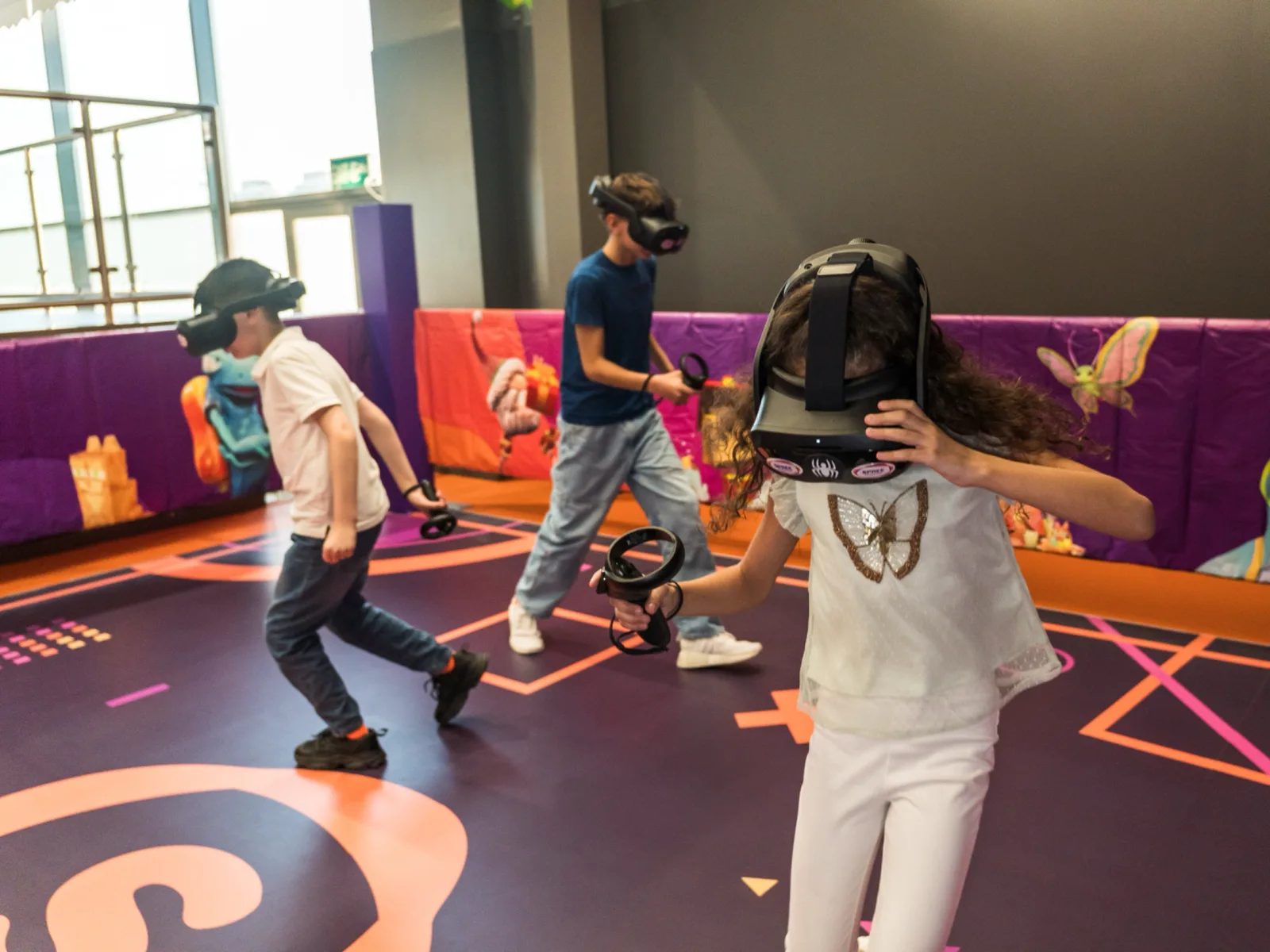 Three kids in VR headsets moving around the free-roam VR arena