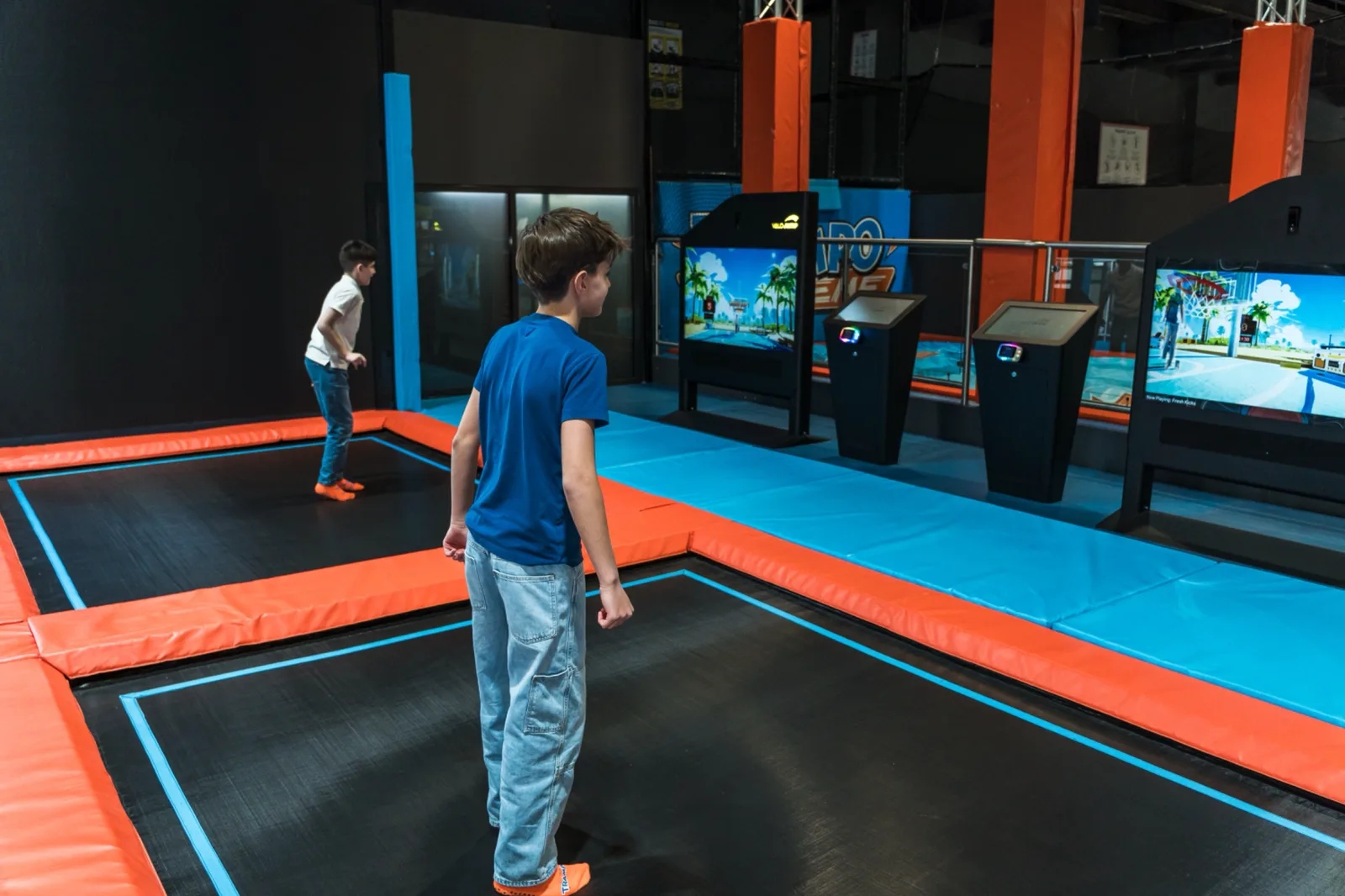 Two boys facing off on adjacent Valo Jump trampoline lanes with the screens running their game